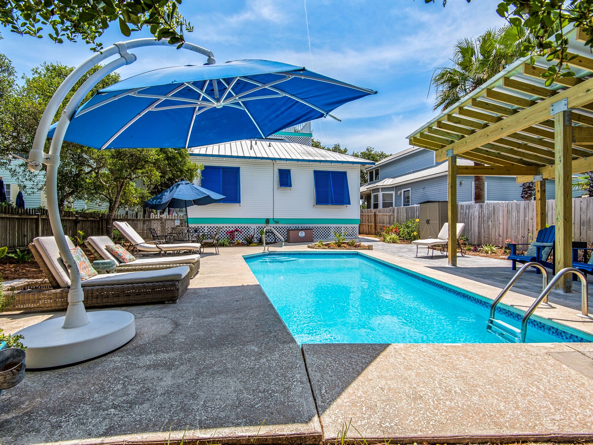 A backyard with a swimming pool, lounge chairs, and umbrellas.