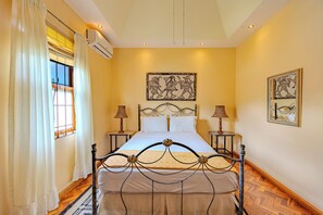 Une chambre à coucher comprenant un lit, deux tables de chevet, une fenêtre avec des rideaux et des œuvres d’art murales.