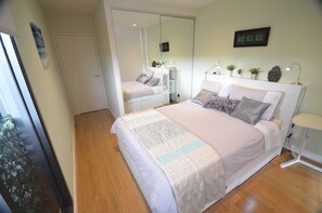 A bedroom with a large bed, bedside tables, a mirror, and a small desk with a lamp. - City Views Riverside 2 Bed/2 Bath Resort apartment (Abbotsford)