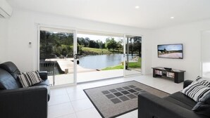 Een moderne woonkamer met een grote schuifpui naar een terras met uitzicht op een meer en groen.