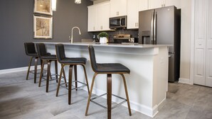 Een moderne keuken met witte kasten, roestvrijstalen apparatuur en een centraal eiland met barkrukken.