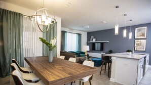Een moderne keuken met een centraal eiland, een eetgedeelte met een houten tafel en witte stoelen, en een zithoek met een bank en gordijnen.