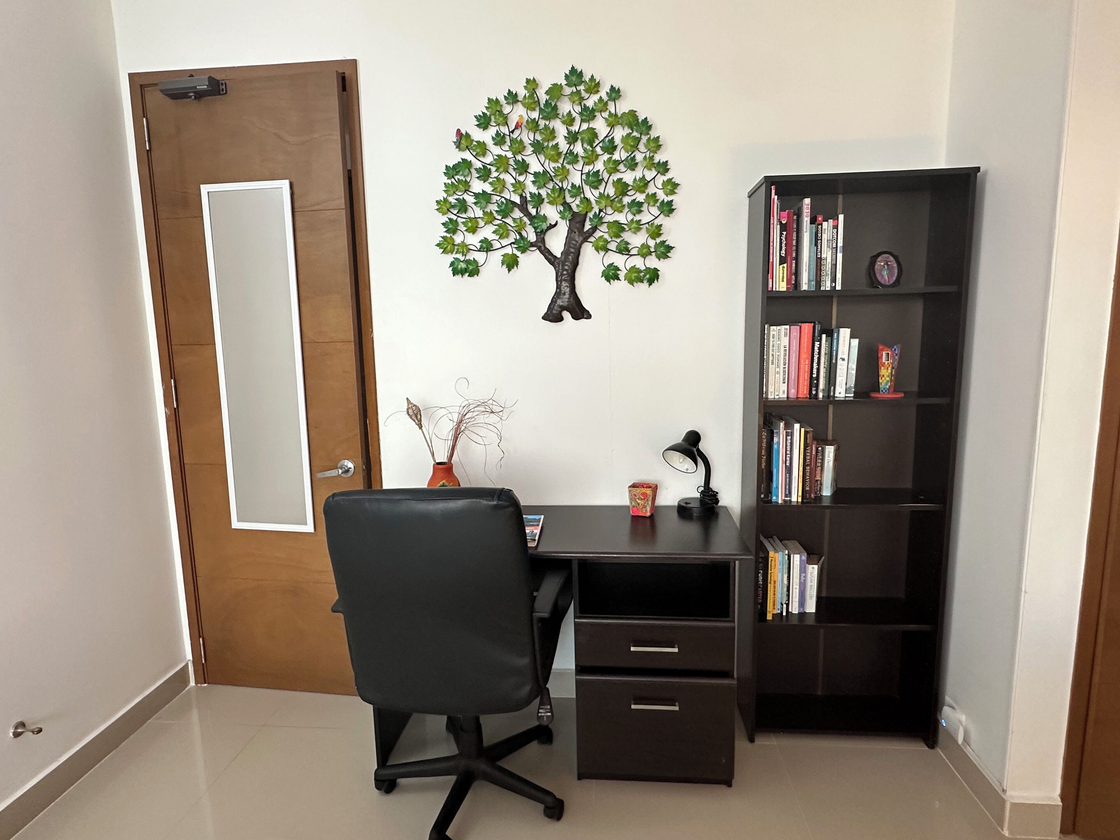 Une salle d’étude équipée d’un bureau, d’une chaise, d’une bibliothèque et d’un arbre décoratif sur le mur.