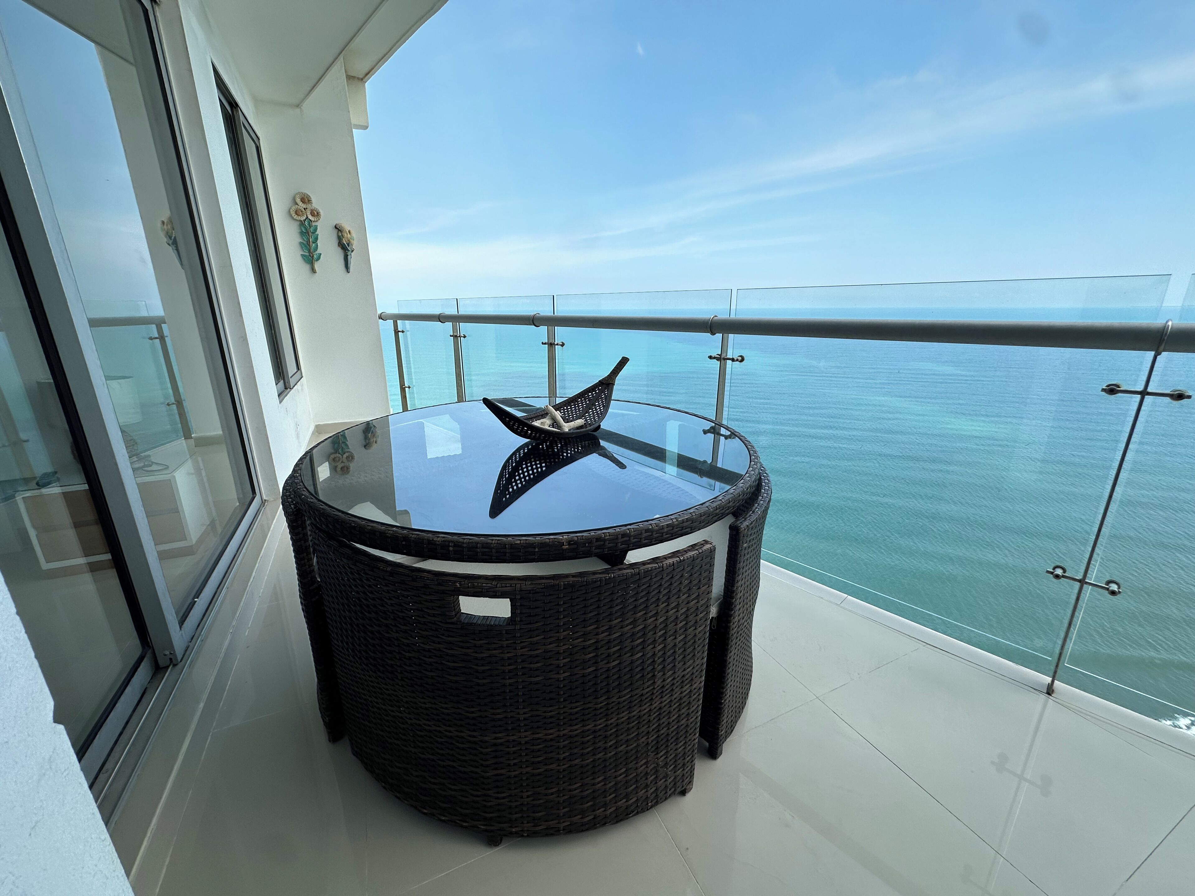 A round glass table with a starfish decoration on a balcony with a glass railing overlooking the sea.