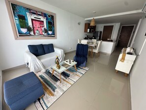 A living room with a sofa, coffee table, and ottoman, a dining area with a table and chairs, and a kitchen with cabinets and appliances.