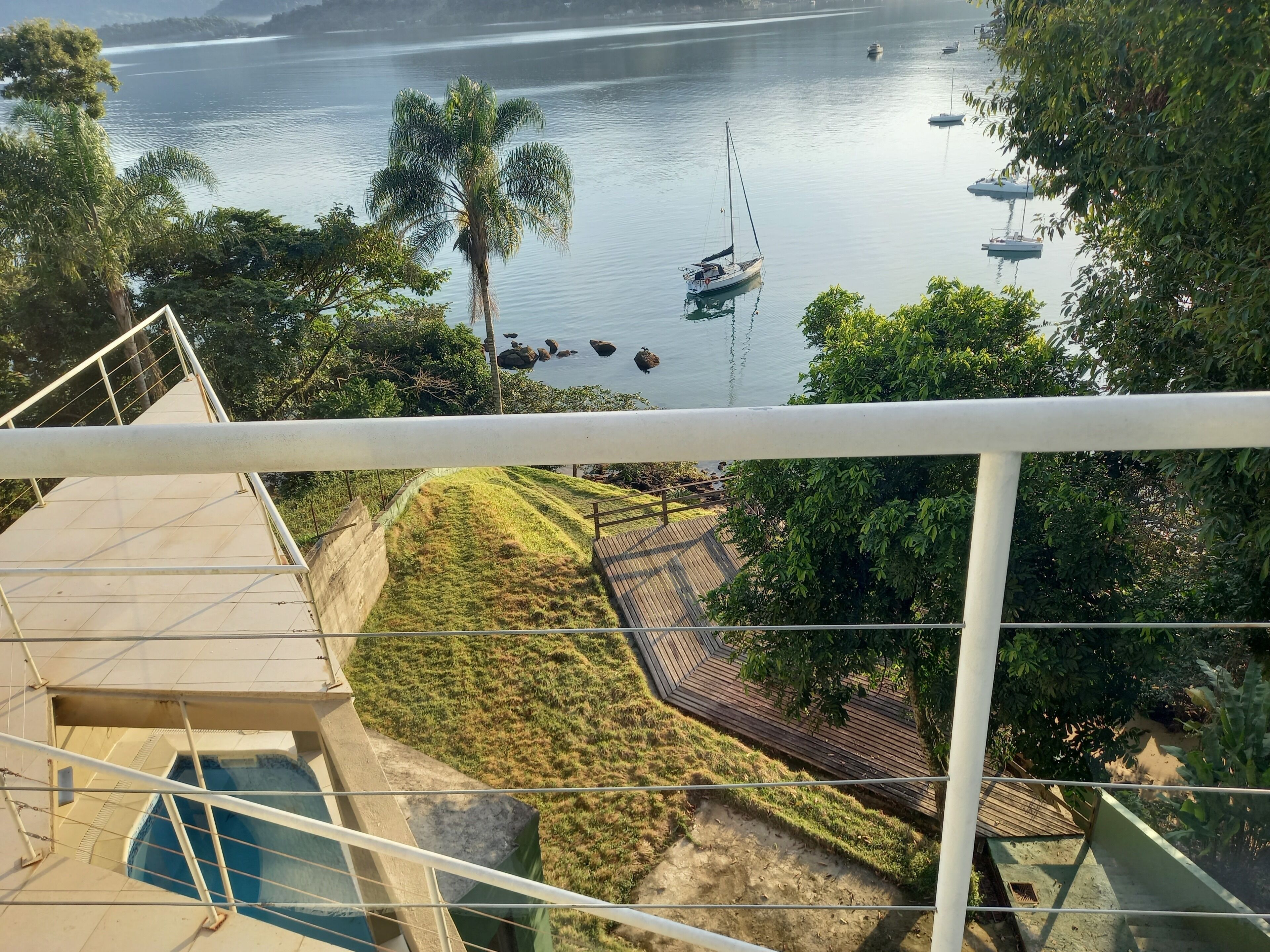 Vista desde un balcón sobre un lago tranquilo con barcos, una palmera y una terraza de madera.