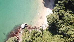 Vista aèria d'una platja amb aigua turquesa cristal·lina, sorra daurada i vegetació verda abundant.