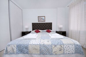 A neatly made bed with a quilt, two pillows, and two folded towels. There is a framed picture on the wall above the bed.