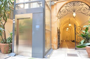 An entrance with a glass door, a metal gate, and a hallway with a light fixture. - SANTA CECILIA APARTMENT (Roma)