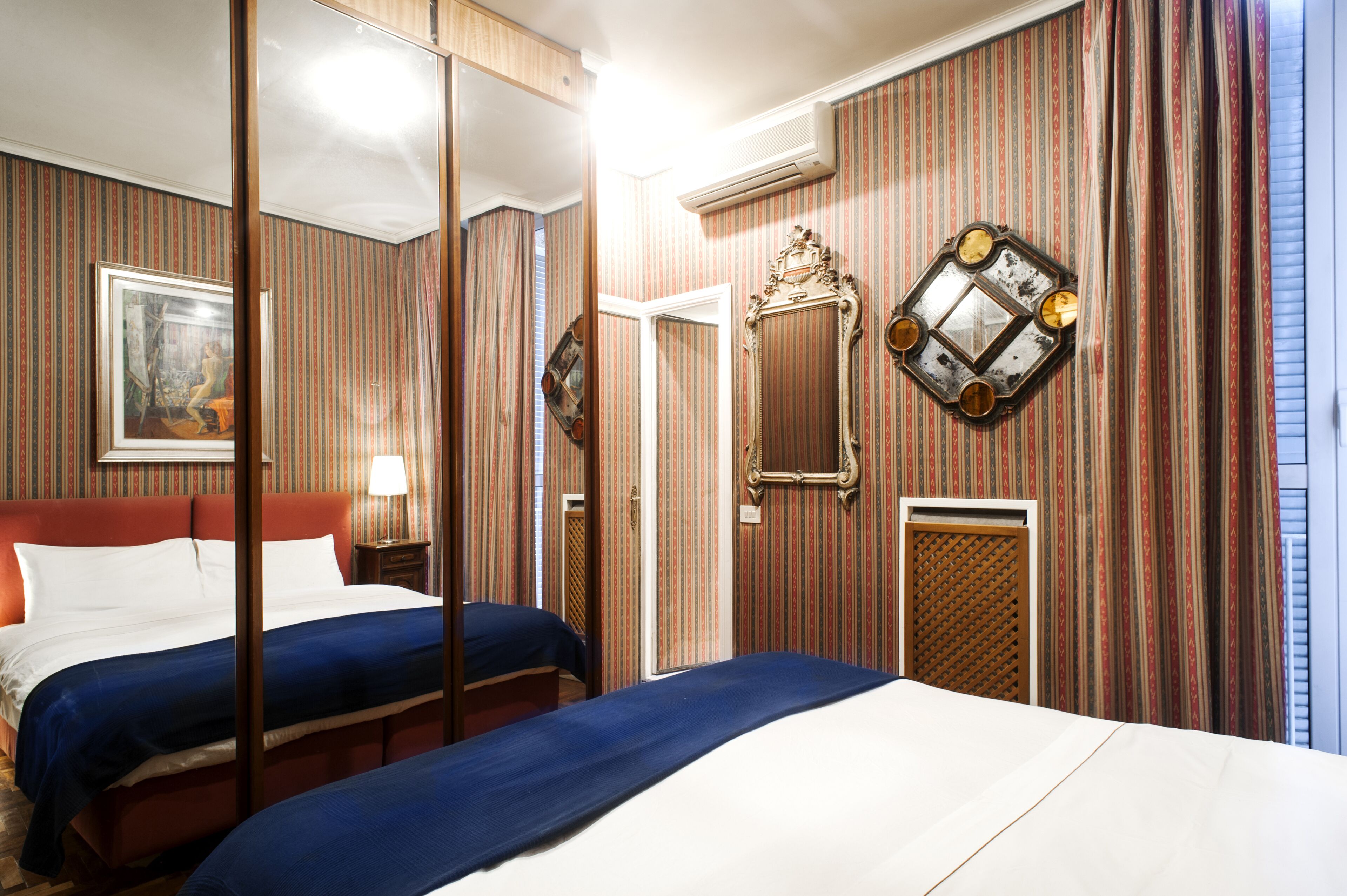 A hotel room with a large bed, a bedside table with a lamp, a mirror, and striped wallpaper.