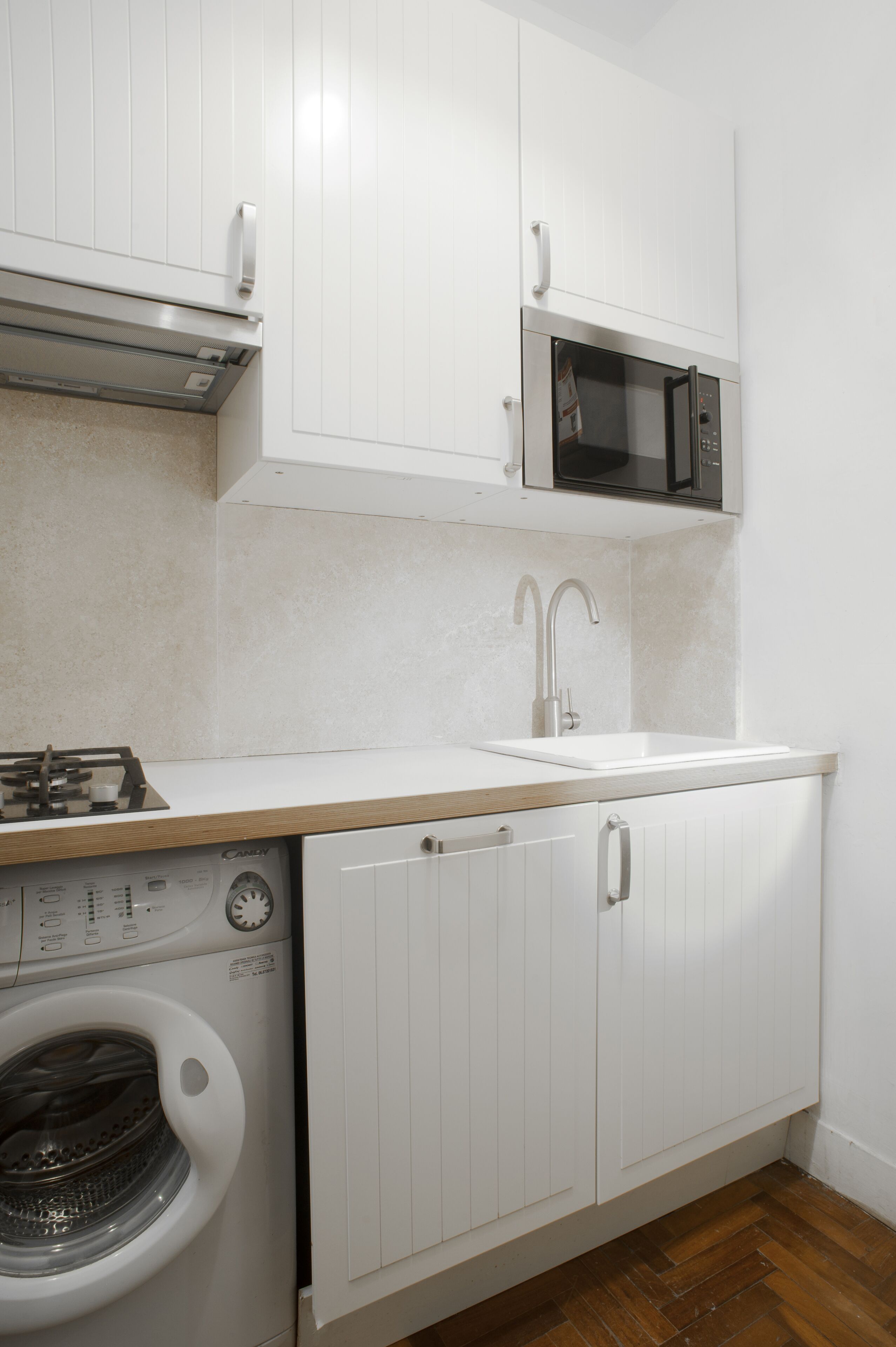 Una cocina compacta con muebles blancos, microondas, lavamanos y lavadora.