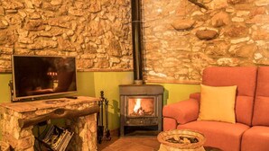 A cozy living room with a stone wall, a fireplace, a television, and a comfortable sofa.