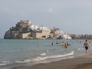 A beach with people swimming and walking, a castle-like structure in the background, and a clear sky. - Self catering L´Amborget y La Mallada for 4 people (San Jorge)