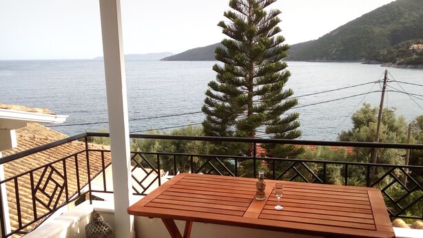 A balcony with a wooden table and chairs, overlooking a body of water and a mountainous landscape. - A penthouse suite in Eptanisa Hotel  (Poros)