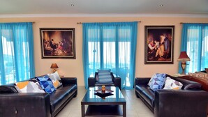 A living room with two black leather sofas, a glass coffee table, and two paintings on the walls. - Elite, Spectacular Villa Enormous HEATED Pool Gym Excellent Location - Sleeps 15 (Argaka)