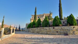A villa with a stone wall, a paved driveway, and tall trees. - Elite, Spectacular Villa Enormous HEATED Pool Gym Excellent Location - Sleeps 15 (Argaka)