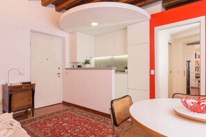 A modern kitchen with white cabinets, a round dining table, and a red accent wall.