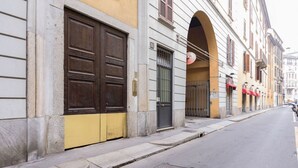 Une rue bordée d’un immeuble caractérisé par de grandes portes en bois, une partie inférieure jaune et une façade en pierre.