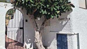 A building with a white exterior, a tree in front, and a gate with the number 16.