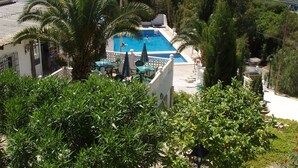 A pool area with a view of the sea, surrounded by greenery and buildings.
