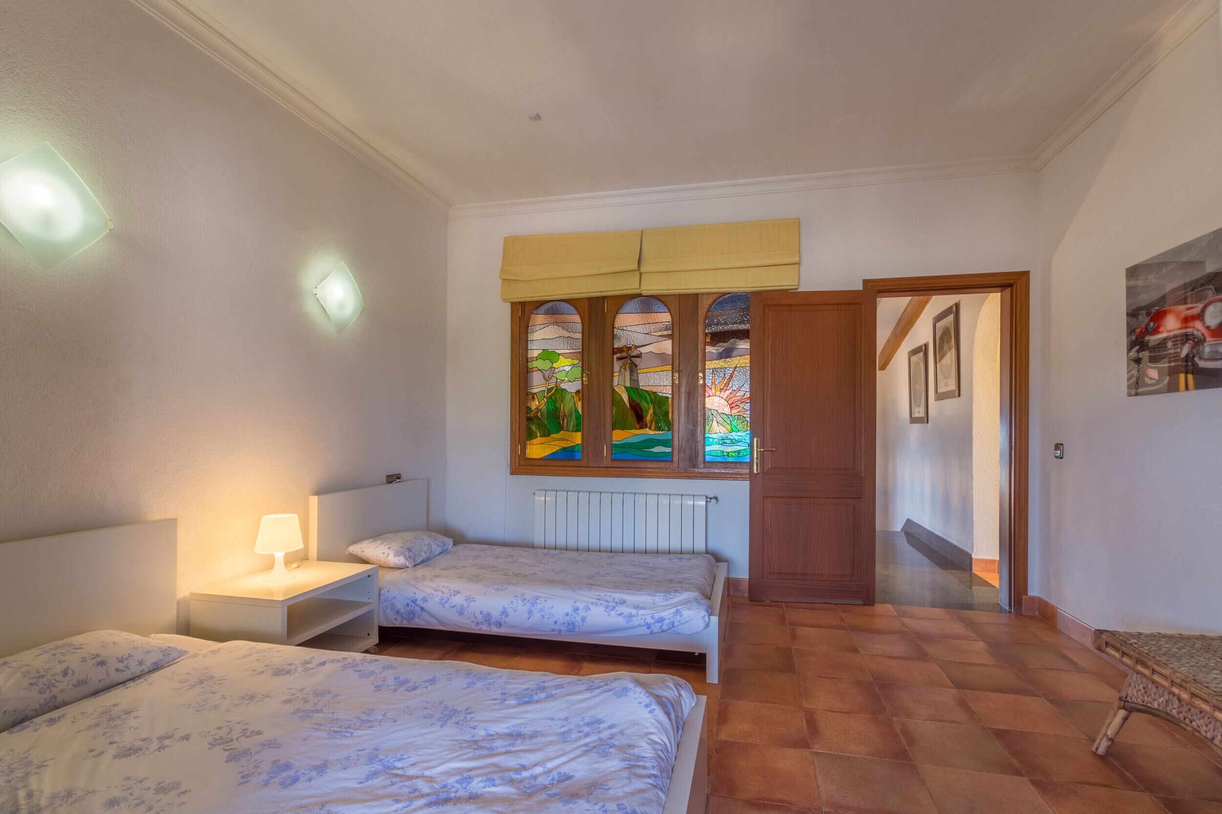 A bedroom with two beds, a nightstand, a radiator, and a window with a view of greenery.