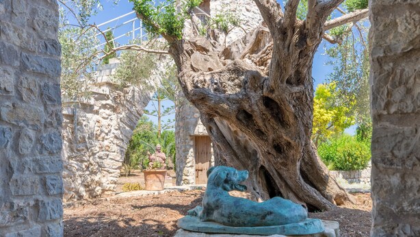 Eine Steinsäule, ein großer Baum und eine Hundsskulptur.