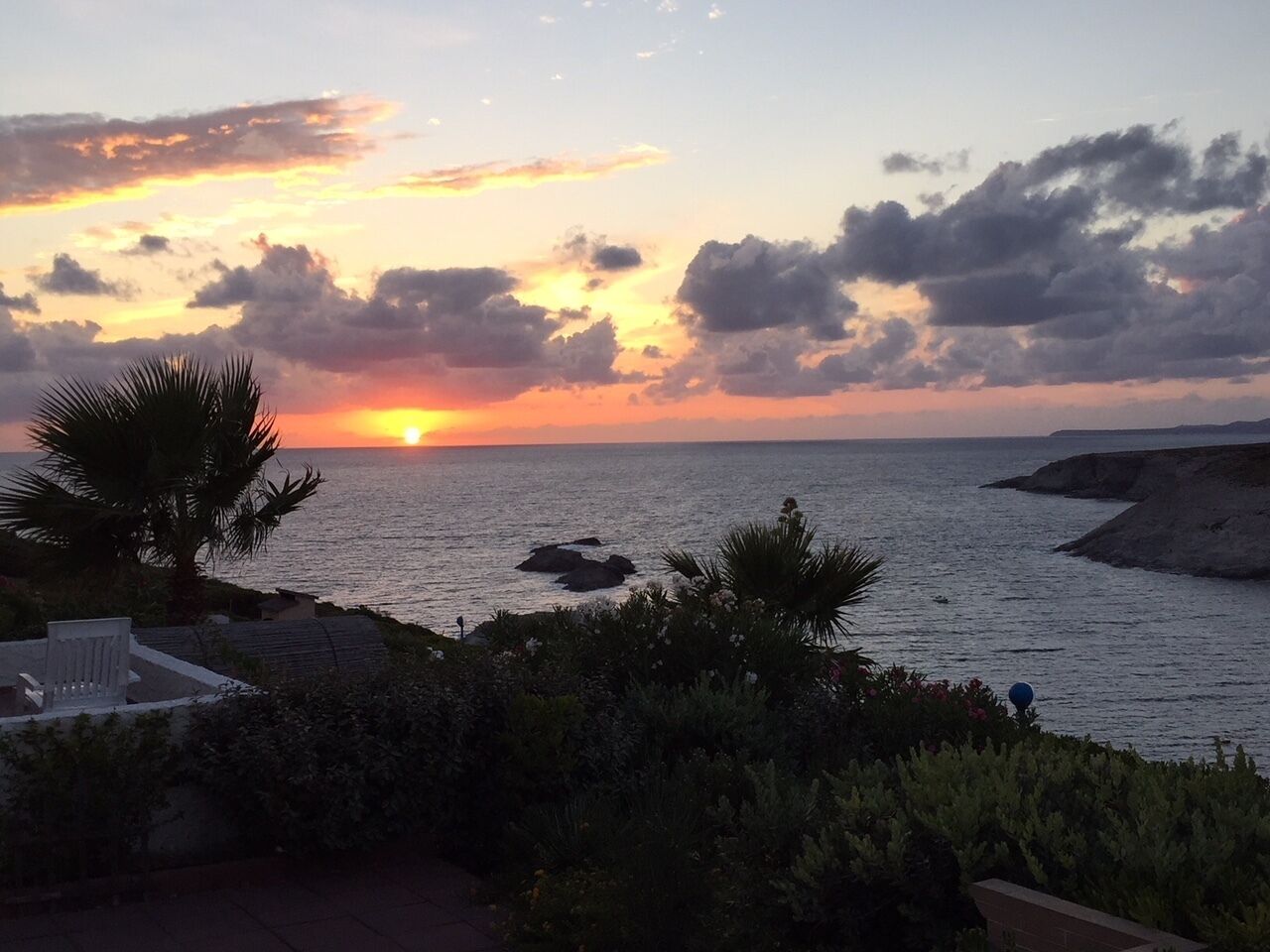 A sunset view over the ocean with a beach and palm trees.