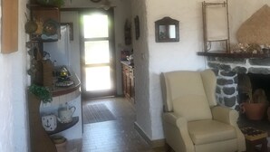 A living room with a stone fireplace, a beige armchair, and a kitchen area with a wooden counter and various decorations. - Terrace with dreamy sunsets over the sea! ( CIN code IT111071C2000T8749) (Sant’Antioco)