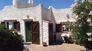 A white building with a rustic, textured exterior and a brick pathway leading to a wooden door. - Terrace with dreamy sunsets over the sea! ( CIN code IT111071C2000T8749) (Sant’Antioco)