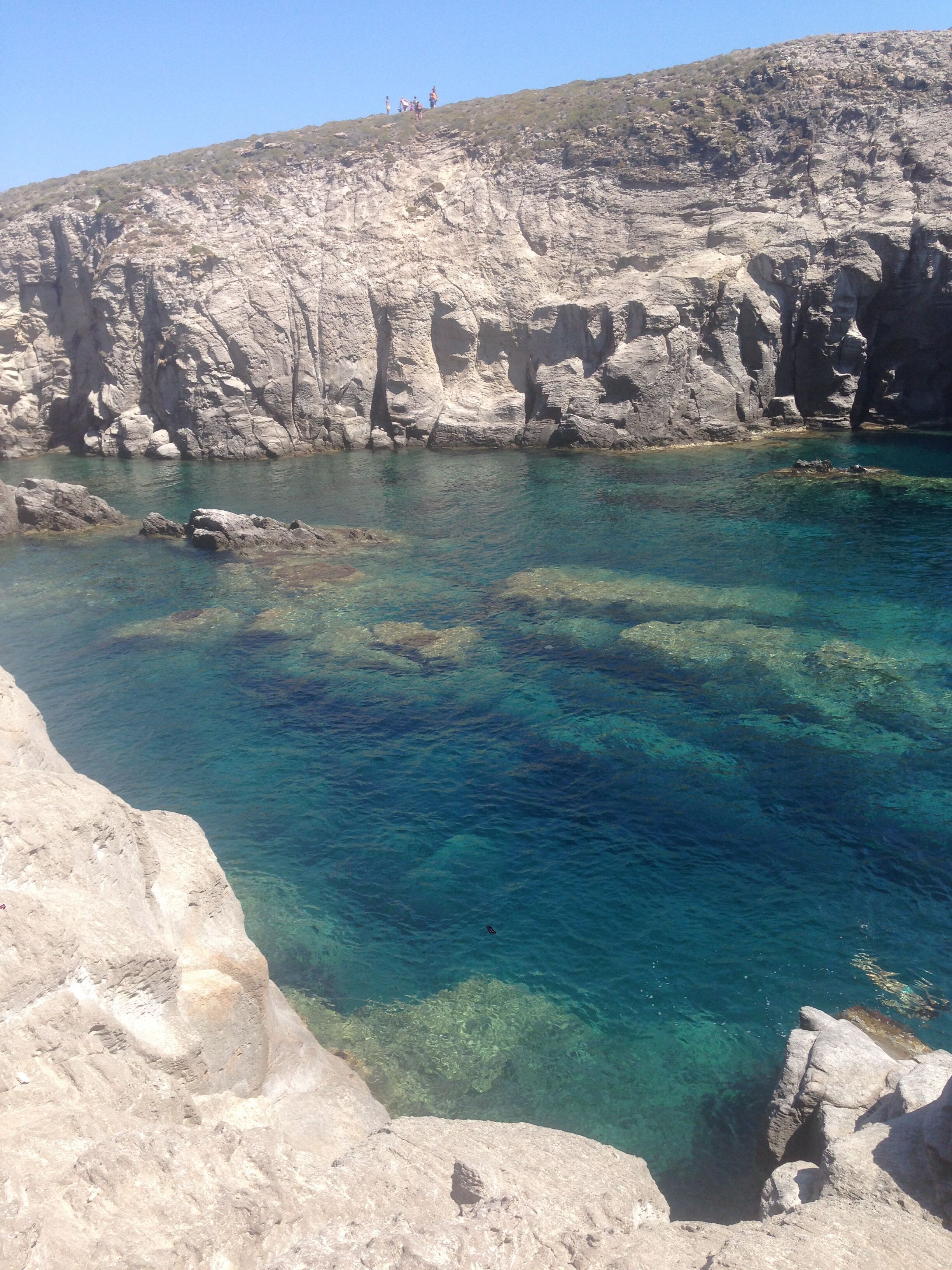 Eine zerklüftete Küstenlinie mit klarem türkisblauem Wasser und einer steilen Klippe.