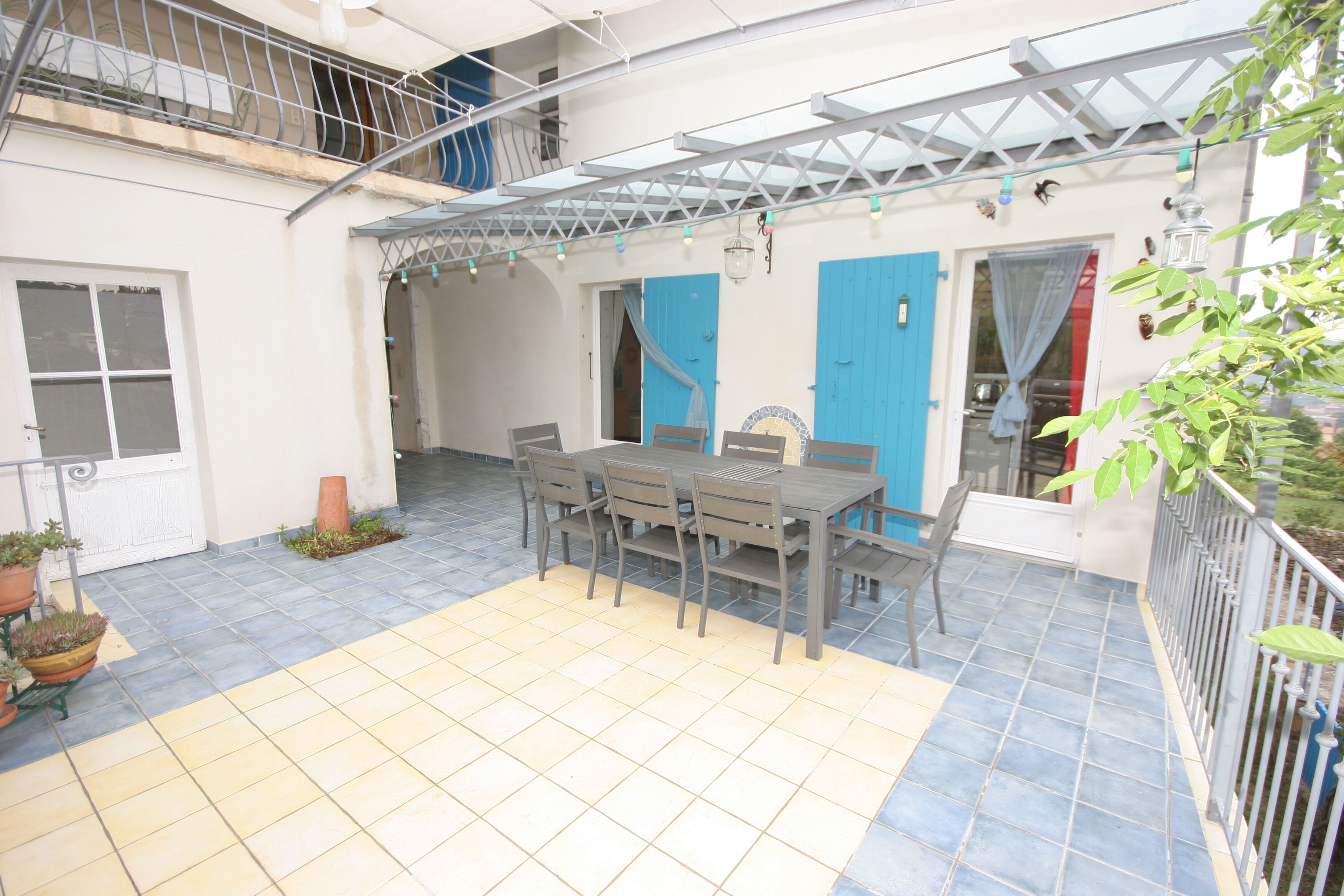 Un patio techado con mesa y sillas, piso de baldosas y un balcón con barandilla.