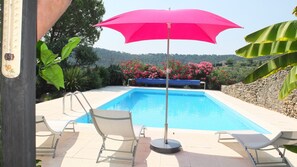 Ein Schwimmbecken mit einem pinken Sonnenschirm, umgeben von Liegestühlen und üppiger Bepflanzung.