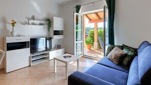 Un salon moderne avec un canapé bleu, un meuble TV blanc et une porte vitrée donnant sur un espace extérieur agrémenté d’une table et de chaises de patio.