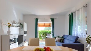 Un salon moderne avec une table à manger, un canapé bleu et une vue sur un jardin, visible à travers une porte vitrée.