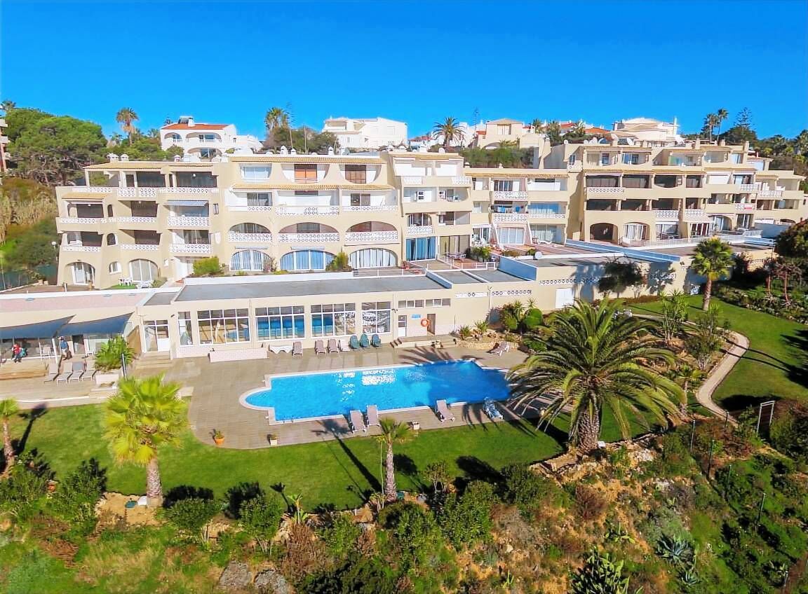 A multi-story hotel with a swimming pool, balconies, and lush landscaping.