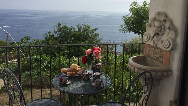 A balcony with a table set for tea, overlooking a sea view.