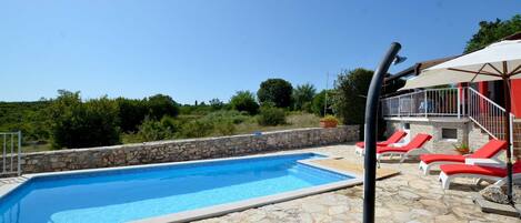 Piscina con baldosas de piedra, sillas reclinables rojas y una pared de piedra.