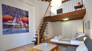 A cozy living room with a wooden staircase, a painting on the wall, and a bed with pillows. - Dala Apartment in Rovinj Centre (Rovinj)