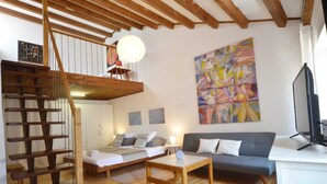 A cozy living room with a wooden staircase, a sofa, a coffee table, and a large abstract painting on the wall. - Dala Apartment in Rovinj Centre (Rovinj)