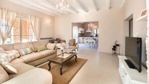 A spacious living room with a sofa, coffee table, and TV. There is a kitchen in the background with a dining area. - Villa San Kirin ***** Lavanda, five stars with Whirlpool, Sauna, billiard ... (Vodnjan)