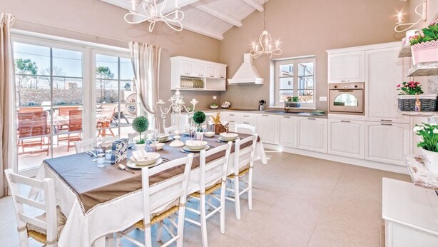 A spacious kitchen with white cabinets, a dining area with a table set for four, and a view of the outdoors through large windows. - Villa San Kirin ***** Lavanda, five stars with Whirlpool, Sauna, billiard ... (Vodnjan)