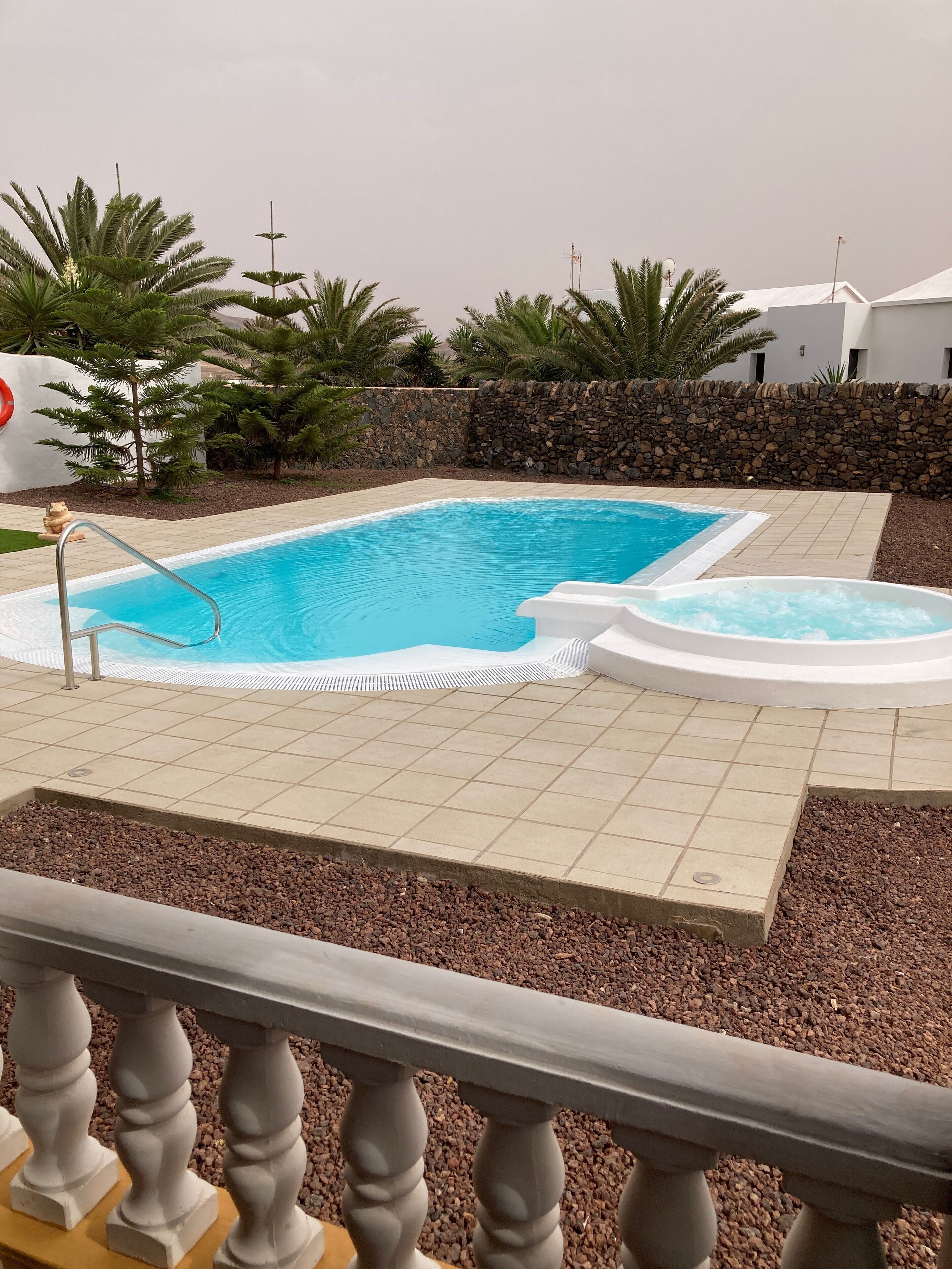 Una piscina con un muro de piedra y palmeras al fondo.