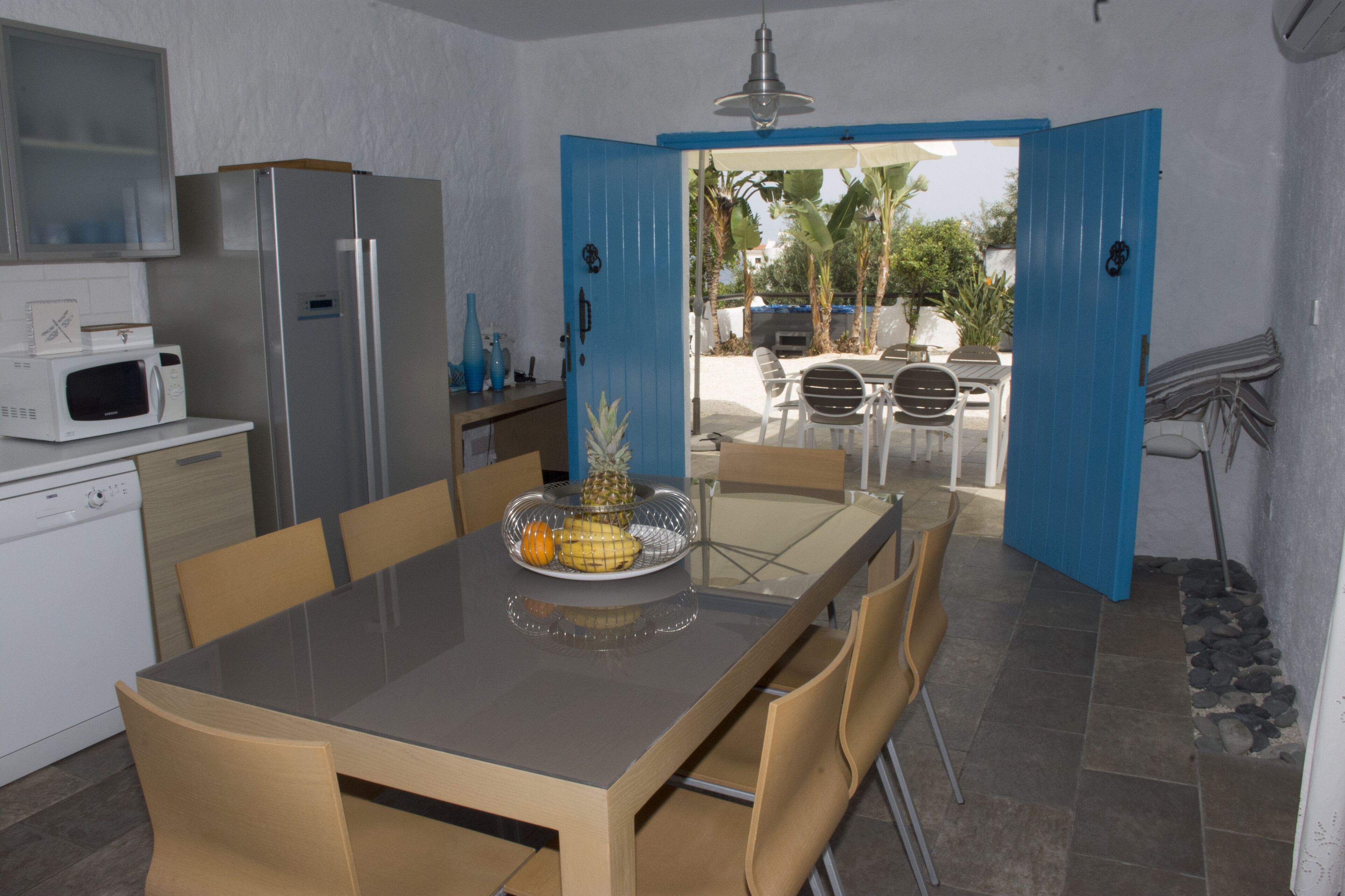 Une cuisine moderne avec un coin repas, comprenant une table à plateau en verre, des chaises en bois, un réfrigérateur en acier inoxydable et un four à micro-ondes.