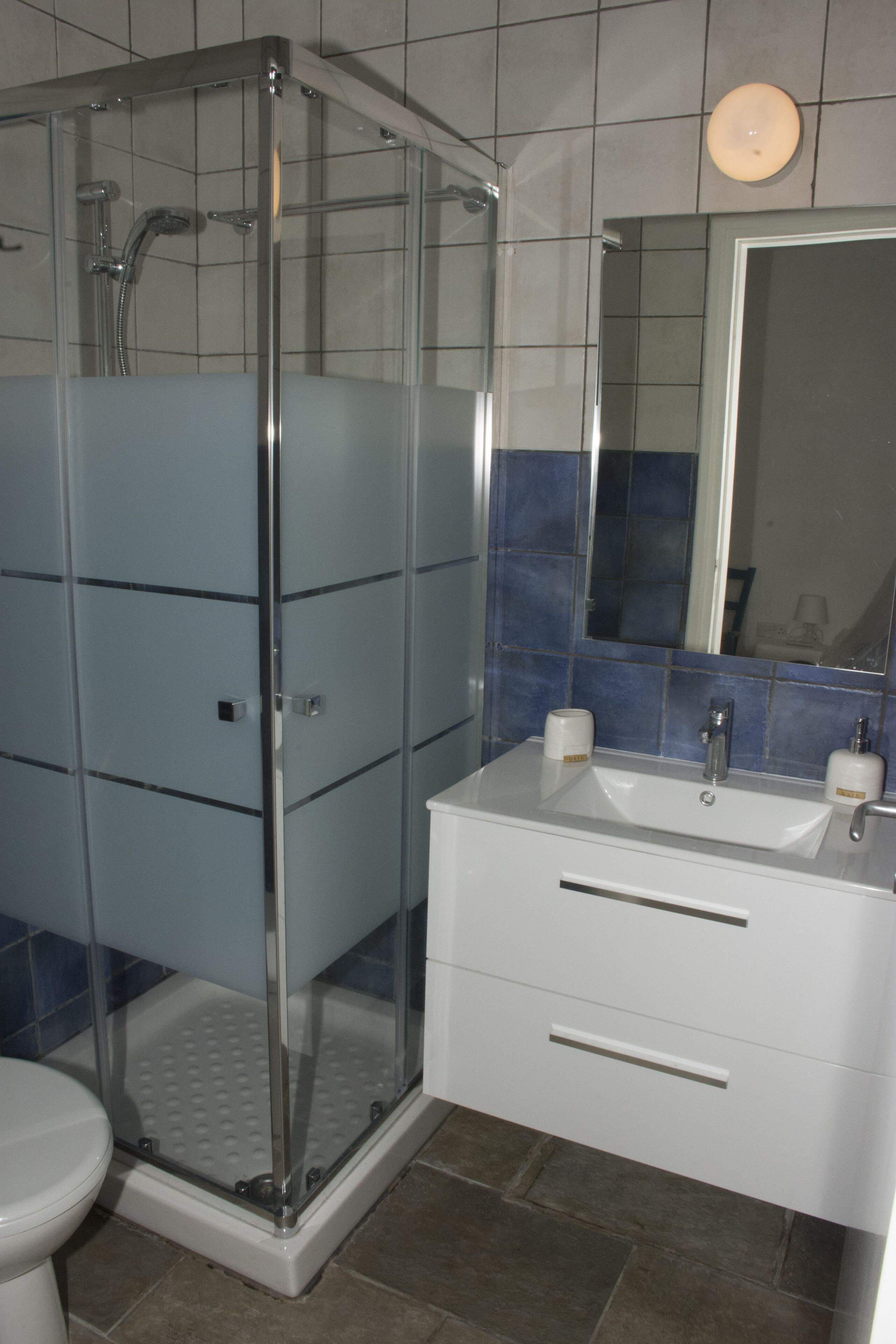 A bathroom with a glass-enclosed shower, a white sink with a mirror above it, and a toilet.
