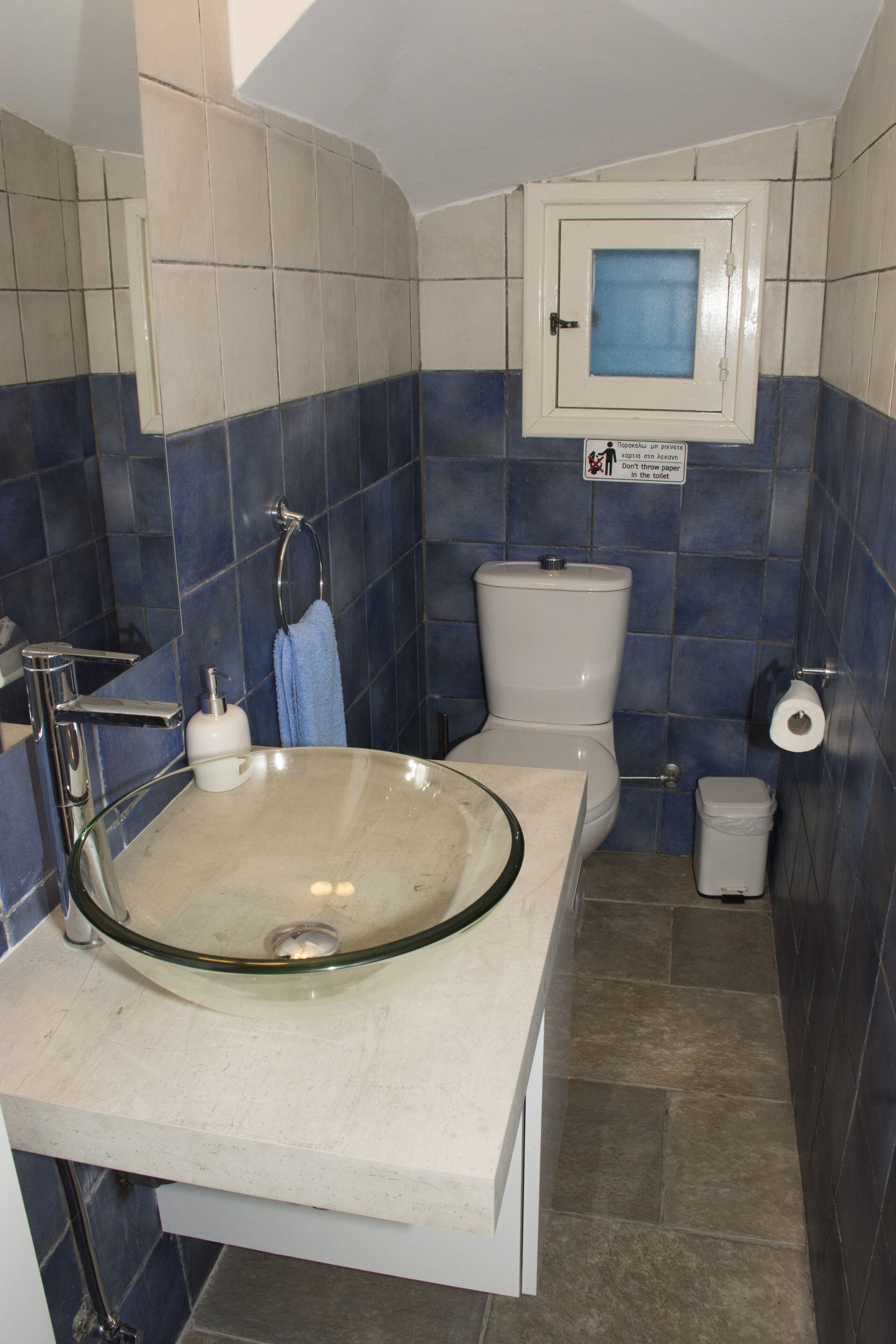 Een badkamer met een glazen wastafel, toilet en een muur betegeld met blauwe tegels.