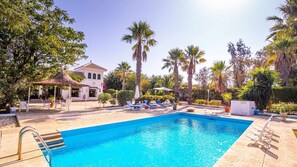 A swimming pool with lounge chairs, palm trees, and a building with a tiled roof. - Santa Ana Holiday Home in Marchena, Seville. (Marchena)