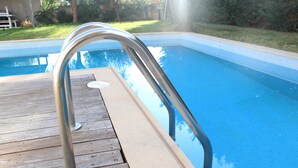 A wooden deck with a metal pool ladder leading into a clear blue pool.