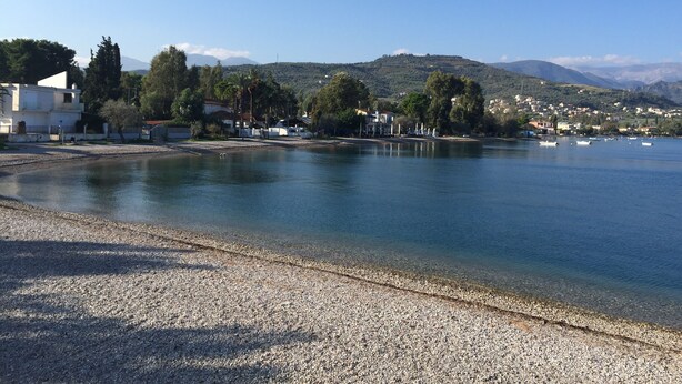 A coastal area with a pebble beach, clear water, and buildings along the shore.