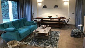 A modern living room with a teal sofa, a wooden coffee table, and a dining area with a bench and chairs.