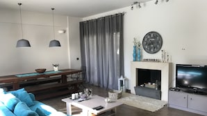 A modern living room with a sofa, a coffee table, a TV, a fireplace, and a dining area with a table and chairs.